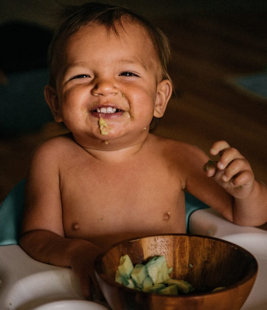Smiling baby eating a bowl of avocado chunks