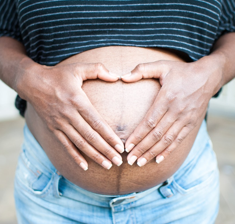 Pregnant person gently holding their belly, symbolizing preparation for breastfeeding.